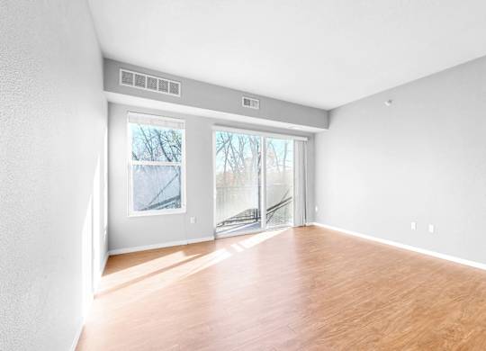 A room with wooden floors and white walls, with a sliding glass door leading outside.