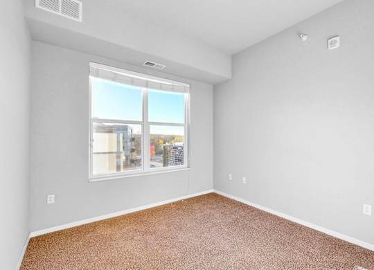 Empty room with brown carpet and a window overlooking a street.