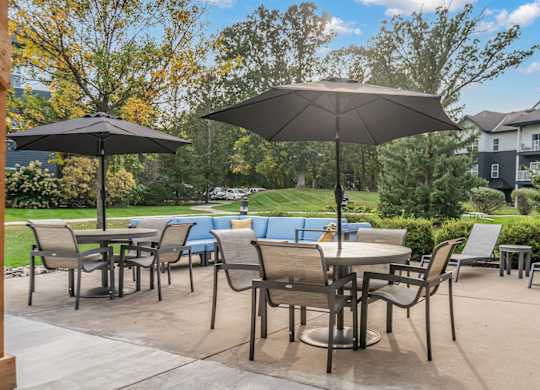 A patio with chairs and umbrellas is surrounded by trees and buildings.