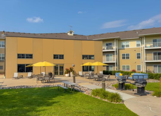 an outdoor patio with tables and umbrellas at chaska place apartments