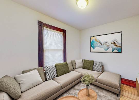 A living room with a grey couch and a painting on the wall.