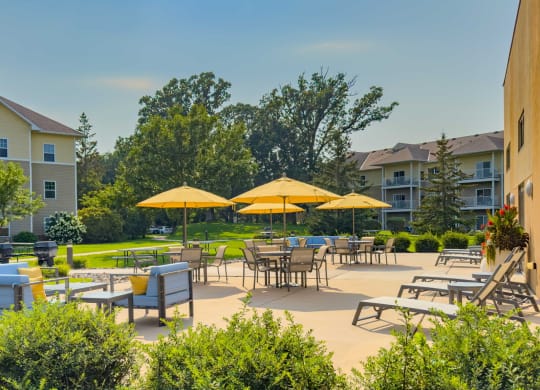 an outdoor patio with tables and umbrellas at chaska place apartments