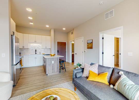 a living room and kitchen with a grey couch and yellow pillows
