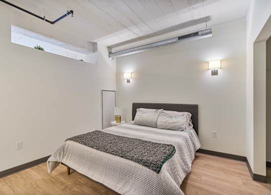 A bedroom with a bed, pillows, and a grey blanket.