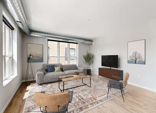 A living room with a grey couch, a rug, a wooden chair and a television.