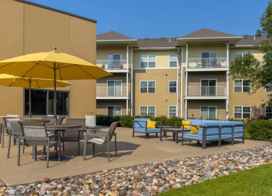 an outdoor patio with tables and umbrellas at chaska place apartments