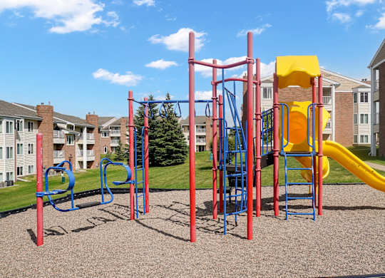 A playground with a red and blue swing set, a yellow slide, and a red and blue jungle gym.