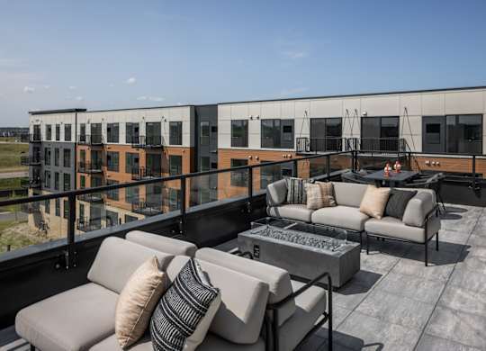 A modern outdoor seating area with a concrete table and grey couches.