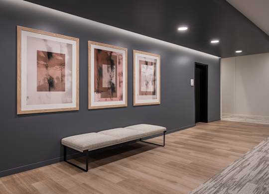 Three framed artworks hang on a wall above a bench in a room.