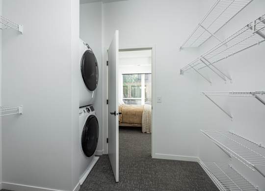 A laundry room with a washer and dryer and a doorway leading to a bedroom.