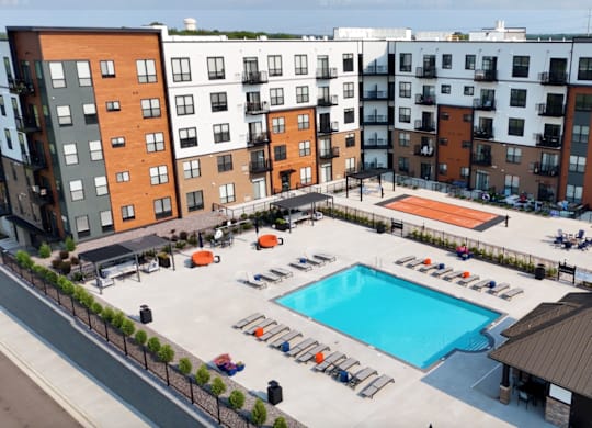 A large swimming pool surrounded by sun loungers and umbrellas in a courtyard surrounded by apartment buildings.