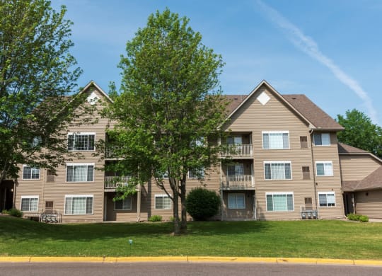 a large apartment building with tan siding and a large tree in front of it