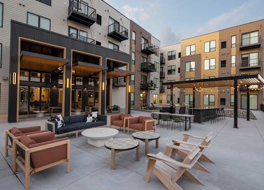 A patio with chairs and tables is surrounded by apartment buildings.