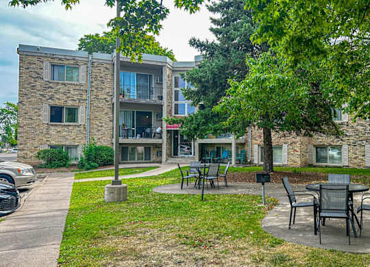 A patio with chairs and a table is surrounded by trees and apartment buildings.