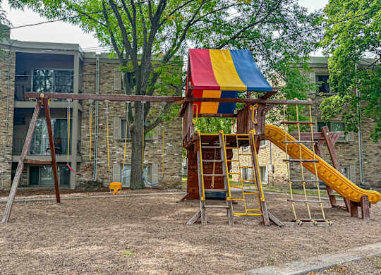 A playground with a yellow slide and a red, yellow and blue canopy.