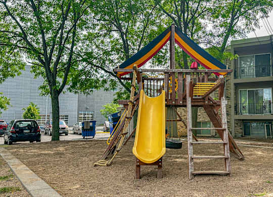 A playground with a yellow slide and a wooden structure.
