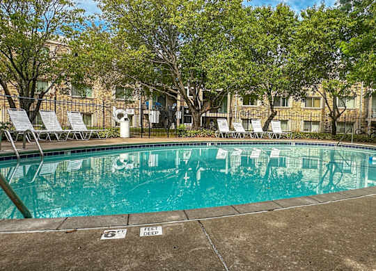 A large outdoor swimming pool surrounded by trees and chairs.