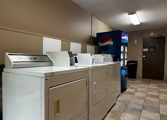 A Pepsi vending machine sits in a room with a white washing machine.