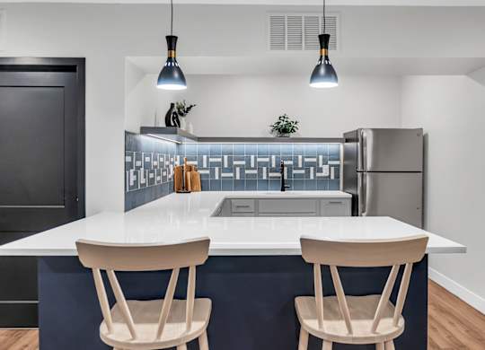 A modern kitchen with a white island and two chairs. at Hillsborough Apartments, Minnesota