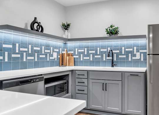 A modern kitchen with a stainless steel refrigerator and a backsplash of blue tiles. at Hillsborough Apartments, Minnesota