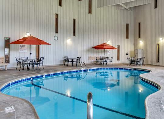 A large indoor swimming pool with a blue tinted water and a white wall in the background. at Hillsborough Apartments, Roseville, 55113