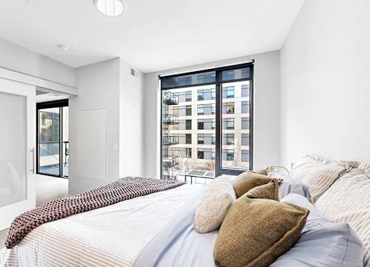 A bedroom with a large bed and a view of a cityscape through the window.