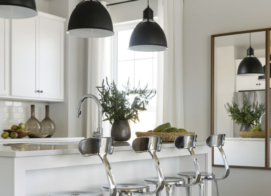 a white kitchen with bar stools and three black lamps