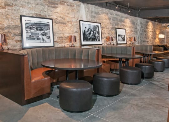 Club Room with Quarter-Circle Booths Around Circle Tables In Front of Exposed Brick Wall at 700 Central Apartments, MN, 55414