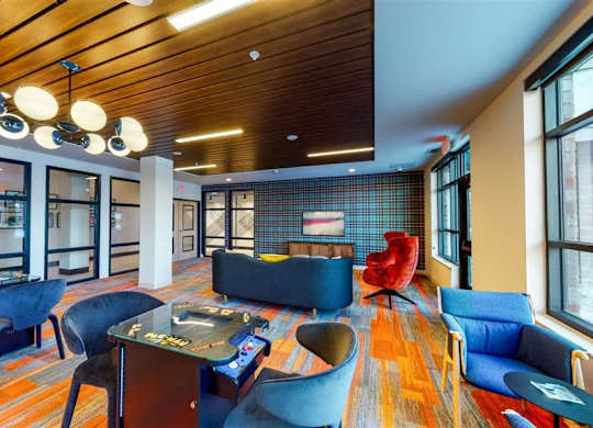 A modern living room with a wooden ceiling and blue chairs at The Bessemer at Seward Commons Apartments, Minnesota