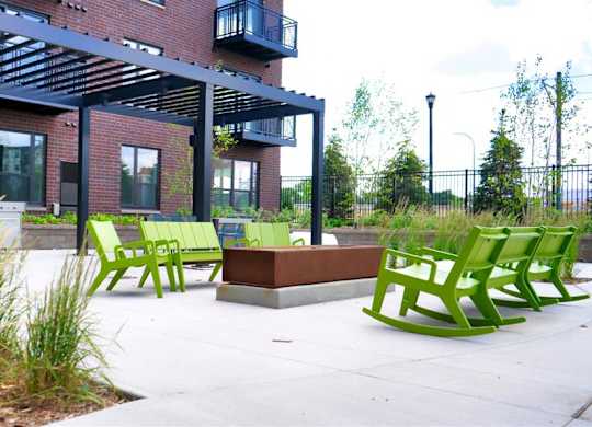 A patio area with green chairs and a bench in front of a building at The Bessemer at Seward Commons Apartments, Minneapolis, MN,  55404