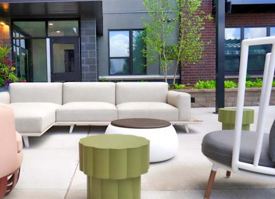 A modern outdoor seating area with a white sofa, green ottoman, and a pink bench at The Bessemer at Seward Commons Apartments, Minnesota