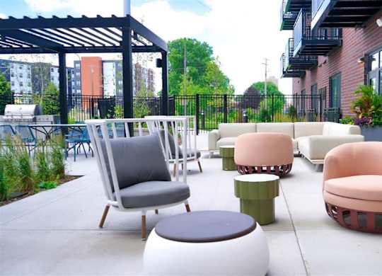 A patio with a black metal awning and a variety of seating options including a pink chair and a round ottoman at The Bessemer at Seward Commons Apartments, Minneapolis, Minnesota