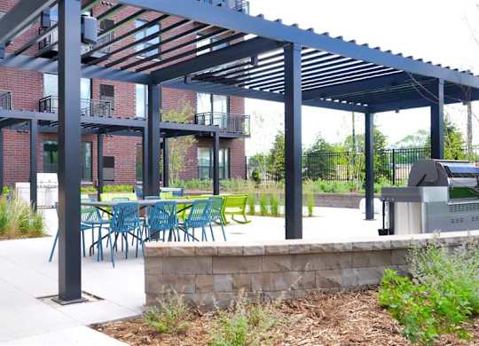 A patio with tables and chairs under a black pergola at The Bessemer at Seward Commons Apartments, Minnesota, 55404