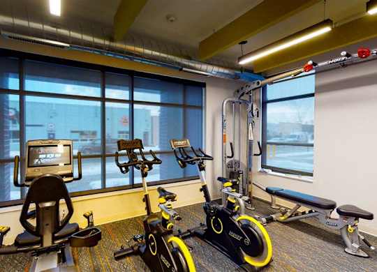 A room with exercise equipment and a window overlooking a city at The Bessemer at Seward Commons Apartments, Minneapolis
