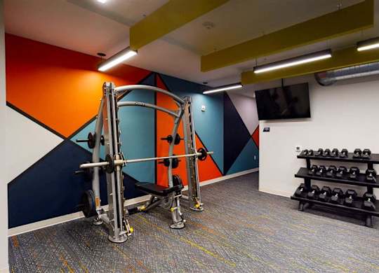A gym with a weightlifting machine and dumbbells at The Bessemer at Seward Commons Apartments, MN, 55404
