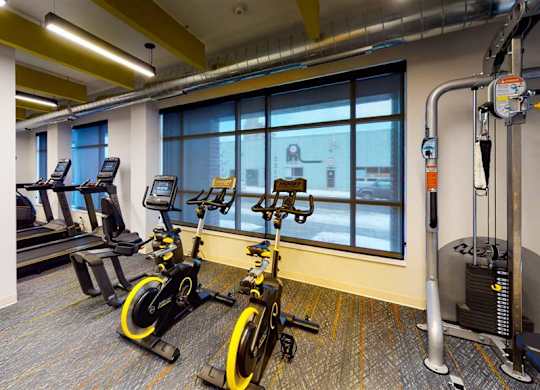 A gym with a row of treadmills and a stationary bike at The Bessemer at Seward Commons Apartments, Minneapolis, Minnesota
