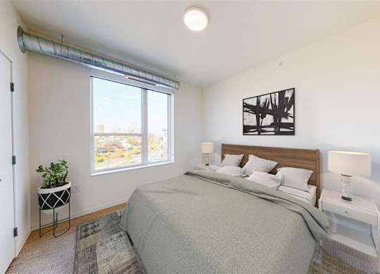 A bedroom with a bed, nightstand, and window at The Bessemer at Seward Commons Apartments, Minneapolis, 55404