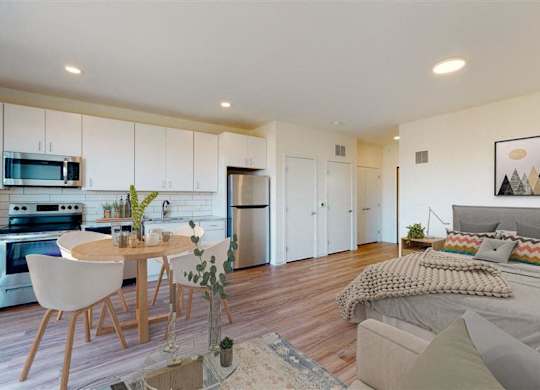 A modern kitchen with a dining table and a bedroom with a bed at The Bessemer at Seward Commons Apartments, Minnesota, 55404