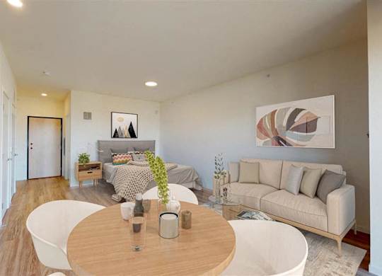 A modern living room with a white couch and a wooden table at The Bessemer at Seward Commons Apartments, Minnesota