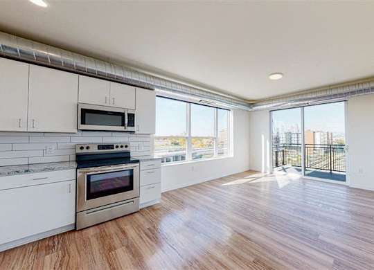 A spacious kitchen with a stainless steel oven and microwave, hardwood floors, and a view of the city through the windows.