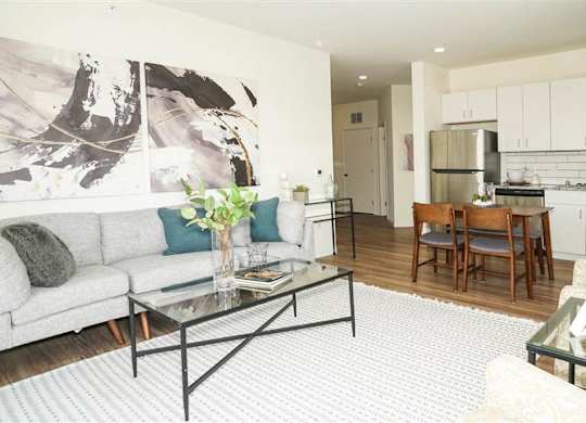 A modern living room with a grey couch, a glass coffee table, and a large abstract painting on the wall at The Bessemer at Seward Commons Apartments, Minneapolis, MN,  55404