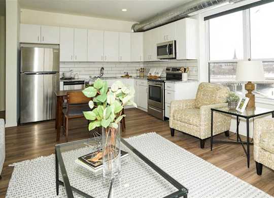 A living room with a glass coffee table and two chairs at The Bessemer at Seward Commons Apartments, MN, 55404