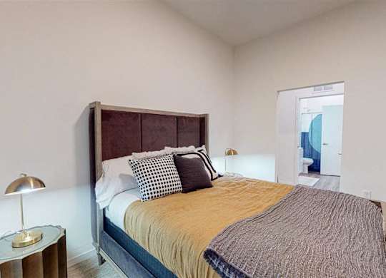 A bedroom with a bed, pillows, and a lamp at The Bessemer at Seward Commons Apartments, MN, 55404
