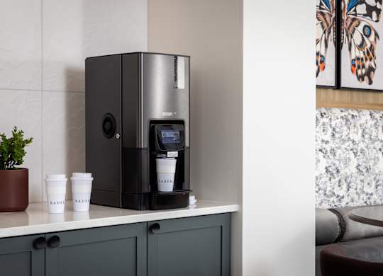 A coffee machine is on a counter with two cups labeled