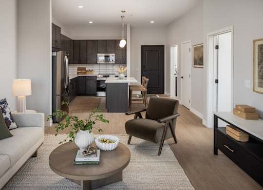 A modern living room with a grey sofa, a coffee table, and a kitchen in the background.