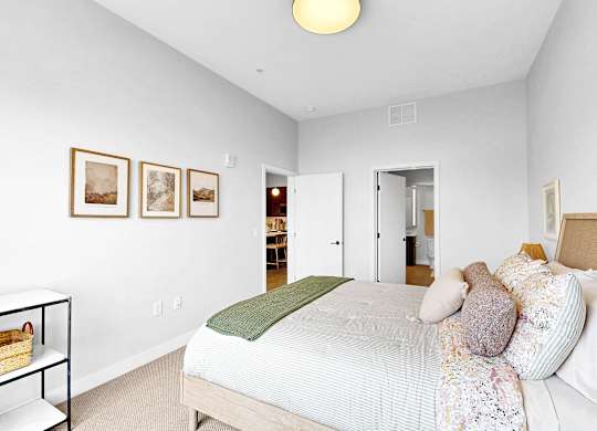 A bedroom with a bed, pillows, and pictures on the wall.