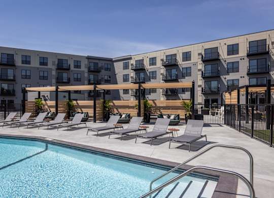 A swimming pool is surrounded by lounge chairs in front of apartment buildings.