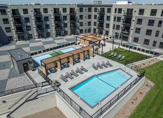 A large outdoor swimming pool surrounded by a black fence and a wooden deck with chairs.