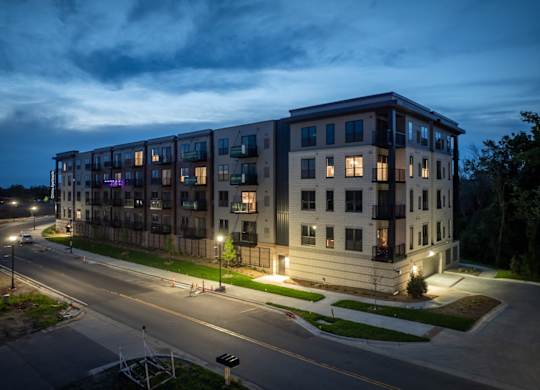A modern apartment building is lit up at dusk with street lights on.