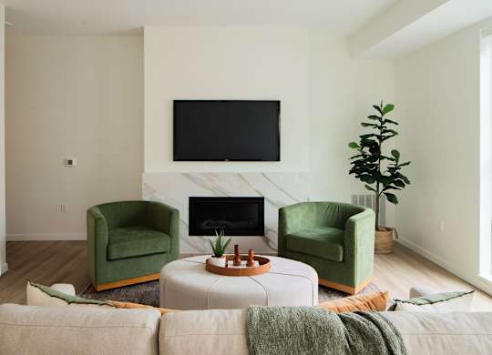 A living room with a fireplace, two green chairs, and a television.
